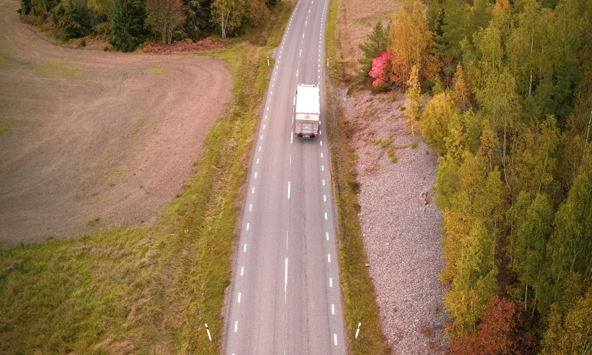 Lastbil på en landsväg genom skog och åkrar, sedd ovanifrån