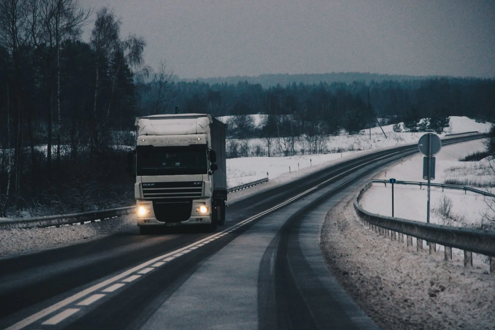 Lastbil på en vinterväg genom ett snötäckt landskap